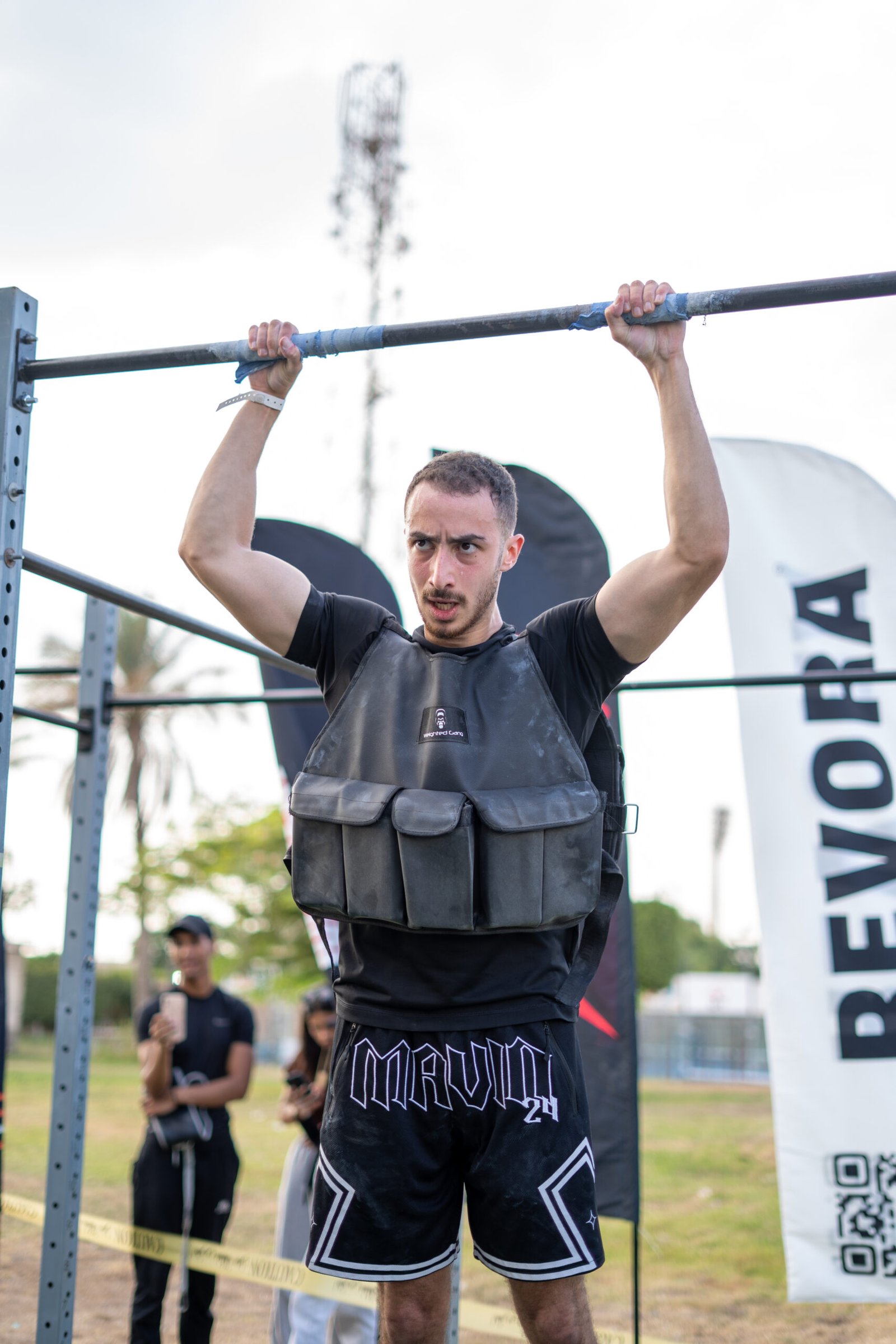 Man lifting barbell with weighted vest during outdoor workout.