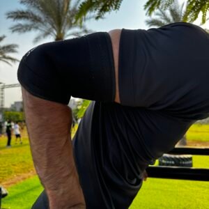 Man with black elbow sleeves exercising outdoors in a park setting.